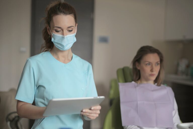 Young female dentist in medical mask and uniform using tablet
