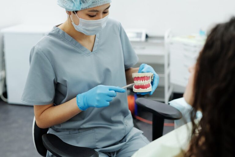 Woman in Blue Scrub Suit Holding Teeth Model