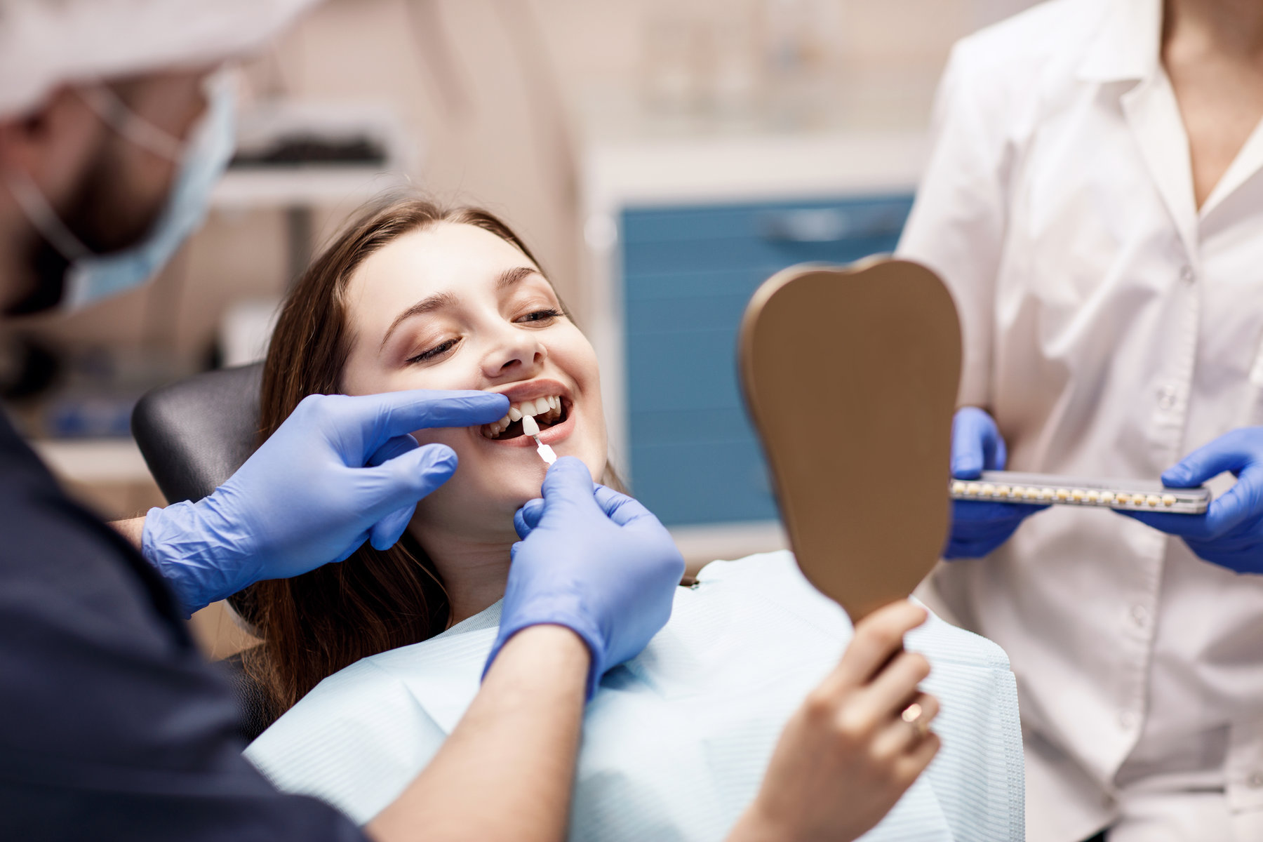 Male dentist comparing patient's teeth shade with samples for bleaching treatment.