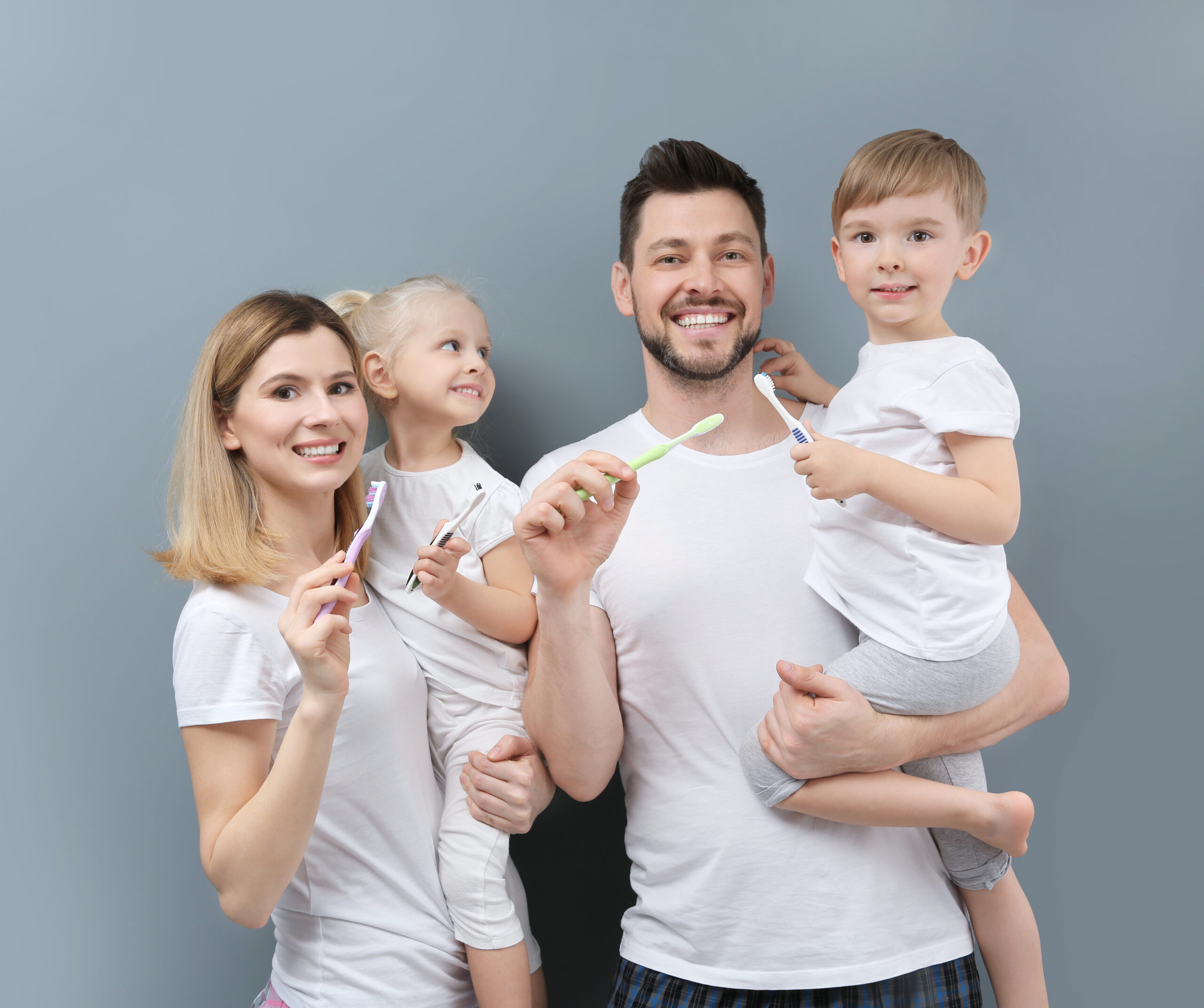 Young family brushing teeth on grey background