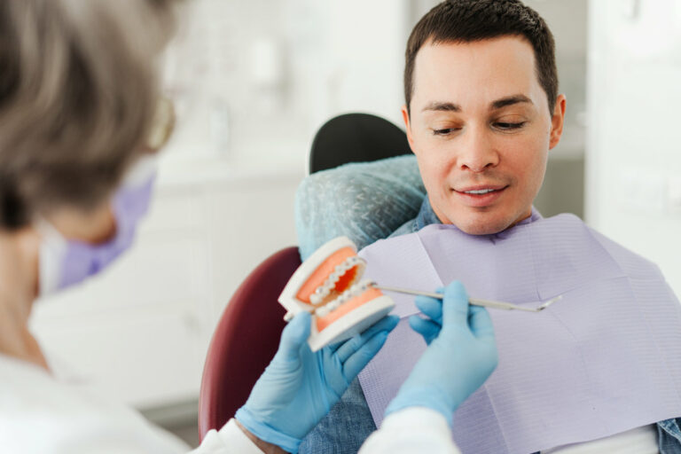 Professional, mature, female dentist, orthodontist holding jaw with braces, talking to patient, explaining something, showing, working in modern dental clinic. Concept of health care, dental treatment