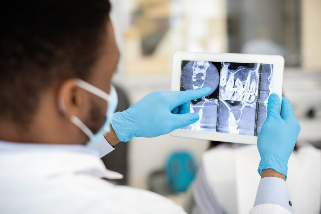 Male Black Dentist Doctor Checking Teeth Xray Picture On Digital Tablet While Working In Modern Stomatological Clinic, Professional Orthodont Looking At Screen With Dental Treatment Result, Closeup