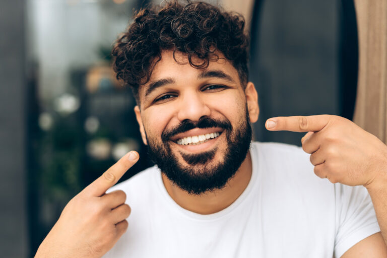 Happy smiling middle eastern man pointing at his white healthy teeth looking at camera. Dental care concept